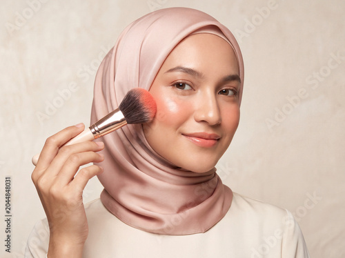 Beautiful Asian Muslim woman in pink hijab applying blush with makeup brush beauty concept