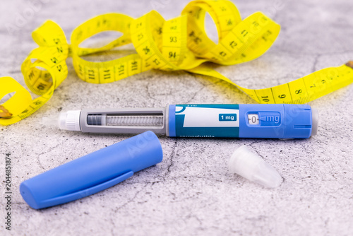 Medical semaglutide glp1 injection pen beside disposable needles and a yellow tape measure displayed on a grey marble background