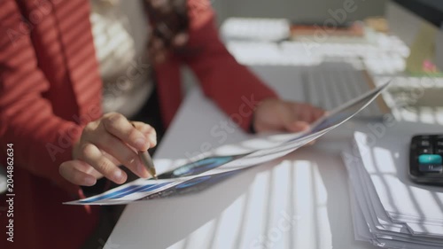 Close up of a female financial analyst reviewing paperwork. Business manager checking documents with charts and graphs at her workplace