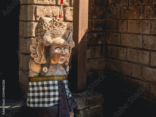 Balinese stone temple guardian statue representing a traditional deity. Wearing a checkered sarong and adorned with frangipani flowers. Indonesia