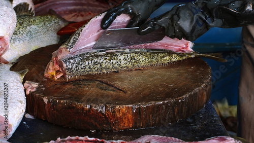 Bild auf Leinwand Close-up of a fishmonger cutting and filleting fresh fish on a wooden chopping block at a traditional seafood market