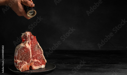 Foto Seasoning raw porterhouse steak with pepper on dark background