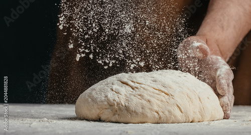 Fotografie Baker dusting bread dough with flour during shaping process
