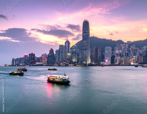 A serene cityscape at dusk featuring a prominent skyscraper-lined waterfront with boats