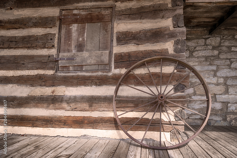Fototapeta premium Rustic old wagon wheel leaned against a log cabin wall.