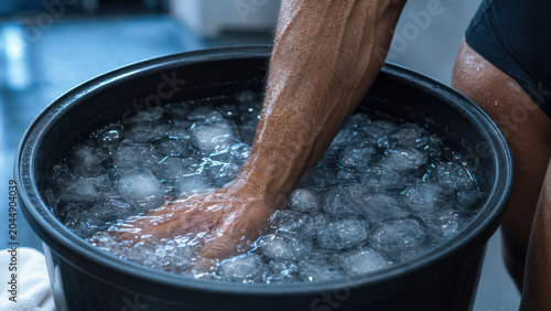 Hand and forearm submerged in ice water recovery bucket, athlete using cold therapy immersion for muscle relief and post workout recovery