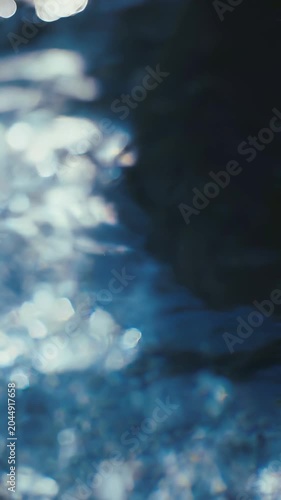 Abstract ethereal blue water surface with shimmering sunlight reflections and dark shadowy depths, evoking a sense of tranquility and mystery.