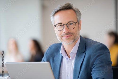 a middle aged man in business attire sits at his desk, a tab in front of him with the background is blurred