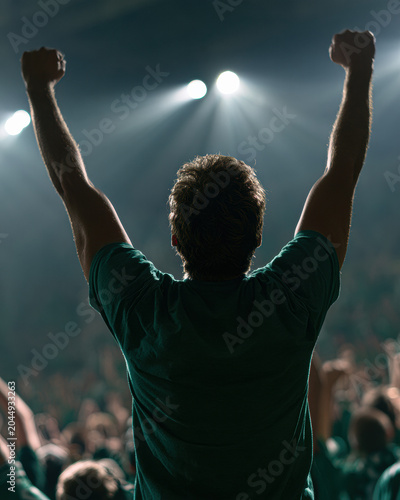 A person raising their fists in celebration or triumph at a crowded event with bright stage lights shining in the background.