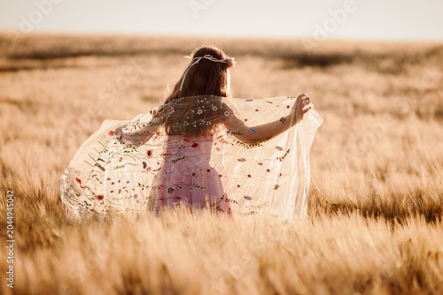 Obraz na płótnie Young Girl Twirling in Floral Dress Among Golden Wheat Field at Sunset