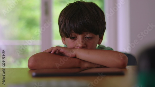 Fényképezés Young boy resting head on folded arms while watching screen on table showing abs