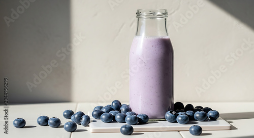 Glass bottle filled with purple blueberry smoothie on white ceramic platter surrounded by loose fresh berries, bright clean studio morning light with sharp shadows, minimalist modern food photography.