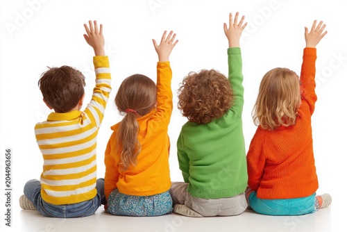 Four diverse children sitting on the floor with hands raised, wearing colorful casual clothes, isolated on a white background, preschool education concept