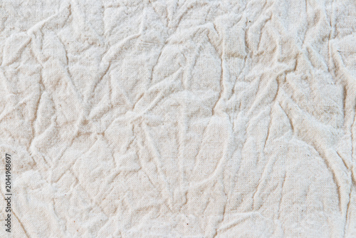 A close-up background texture of crumpled and wrinkled natural beige linen fabric with rustic textile weaves