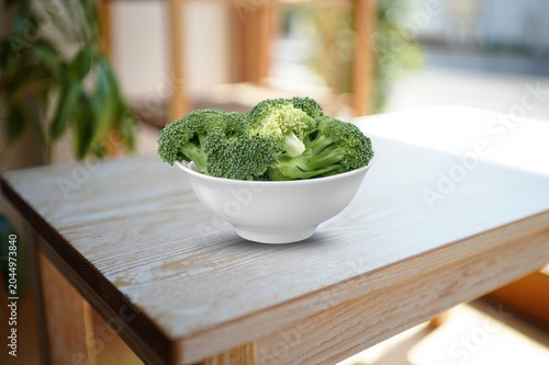 Photos Broccoli florets in a white bowl on a wooden table in a bright room