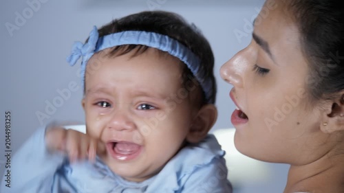 An attractive female nurse holding a little crying baby girl - Baby in tears  crying toddler. A cheerful Indian mother holding and cuddling her sweet infant - parent-child bonding  unhappy  consoli...