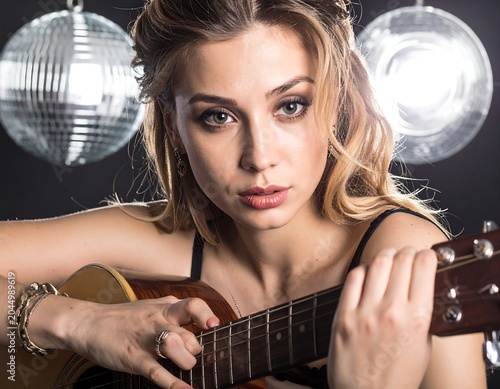 A young woman with blonde hair playing a guitar in a disco-lit room