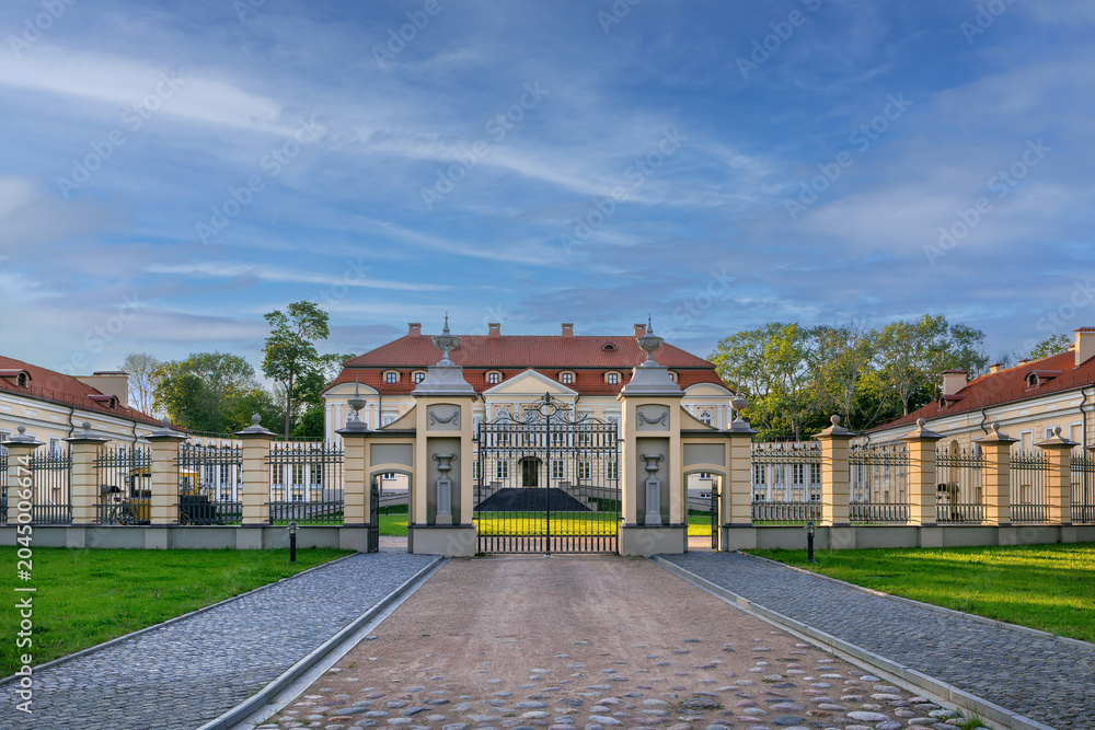 Fototapeta premium Volovich palace view through fence in Svyatsk, Belarus. Baroque and classicism architecture under bright clear blue sky