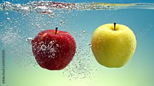 Red and yellow apples splashing into clear water with rising air bubbles against a blue and green gradient background, showing high-speed motion underwater and liquid surface.