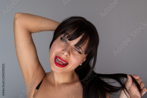Photos Playful young attractive woman in a dark wig winking and sticking out her tongue while holding a strand of hair