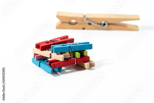 A square arrangement of colorful blue, green, and red wooden clothespins with one large natural wooden clothespin lying in the background on a clean white background