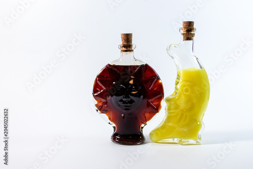 Two glass bottles shaped like the sun and the moon, filled with an amber and a yellow drink, isolated on a clean white background