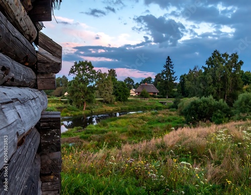 Rustic Wooden Cabin Overlooking Green Meadow and Pond at Dusk