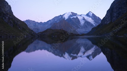 Twilight Reflection of Snow-Covered Alpine Peaks and Cabin on Calm Mountain Lake