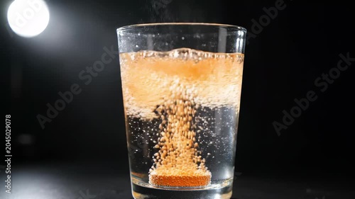 A hand drops a vibrant effervescent tablet into a glass of clear water, unleashing a captivating dance of bubbles and sparkling patterns that swirl and rise, mesmerizing viewers with every moment.