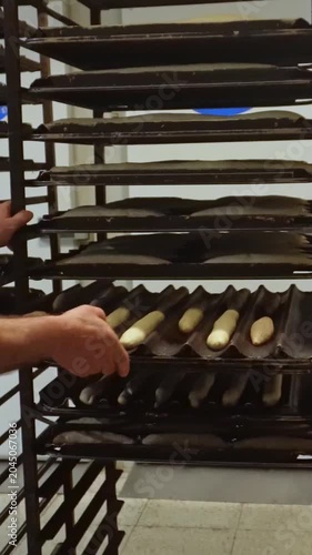 Male baker placing a tray of raw baguette dough onto a metal cooling rack in a professional kitchen before baking in the oven