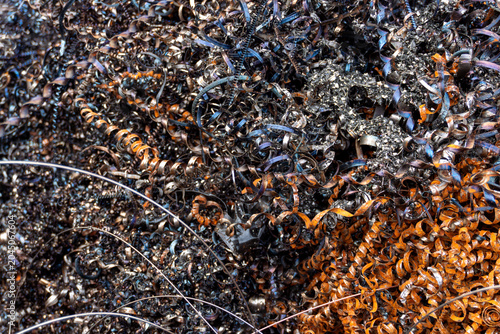 Close-up of curled metal shavings with blue, silver, black, and rust orange tones. Detailed industrial texture for machining, metalworking, recycling, factory waste, scrap material, and manufacturing 