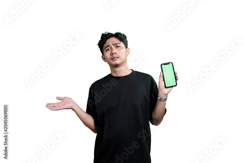 A young Asian man holding a smartphone with a green screen mockup while smiling at the camera. Isolated on a light gray background with copy space. Concept of mobile application promotion, digital mar