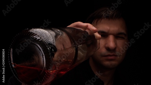 Tableau sur toile Man holding a bottle of dark alcohol, pouring a drink and reflecting on feelings