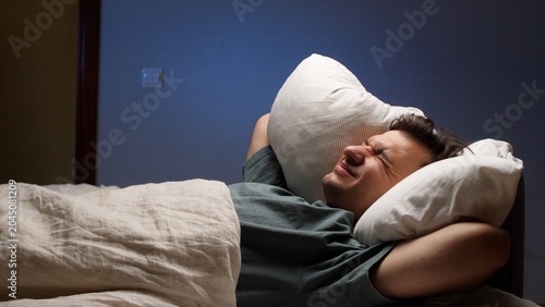 Foto Young man lying in bed experiencing sleep disturbance and insomnia due to noisy
