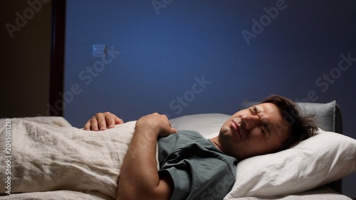 Slika na platnu Man lying in bed with eyes closed, experiencing discomfort and difficulty sleepi