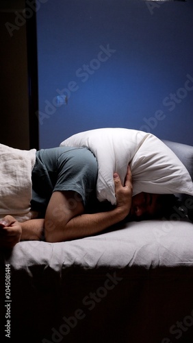 Принти на полотні Man finding no sleep in bed, covering his head and ears with a pillow to block o