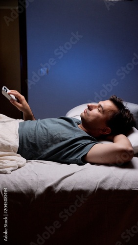 Φωτογραφία Man lying awake in dark bedroom late at night, restless and tired, clutching a r