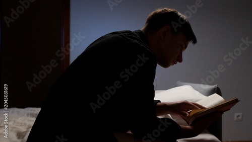 Φωτογραφία Young man reading a book in a dim bedroom at night, focused and peaceful in soli
