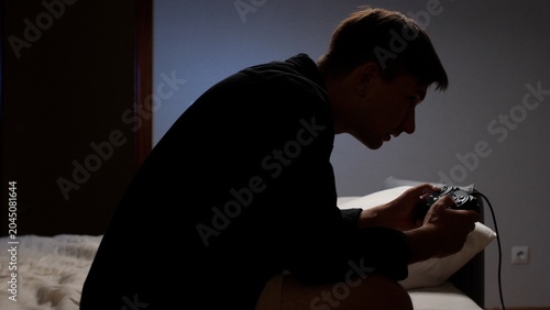 Konstfotografi Young man engrossed in playing video games with a controller, sitting on a bed i