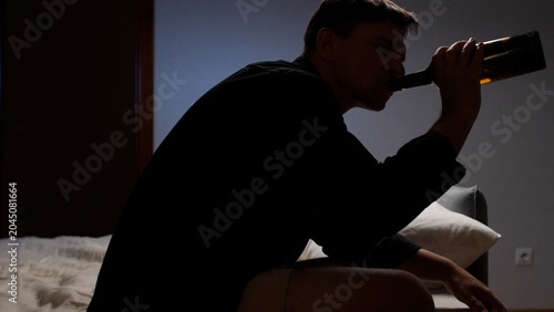 Schilderij op canvas Man in silhouette consuming alcohol directly from a bottle, sitting indoors in a