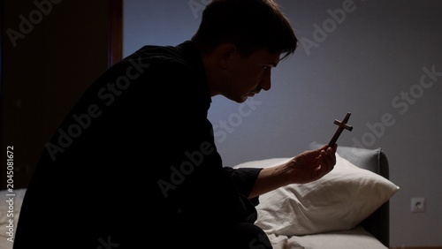 Fotografie Man in a dim room holding a small wooden cross, quietly praying and reflecting o