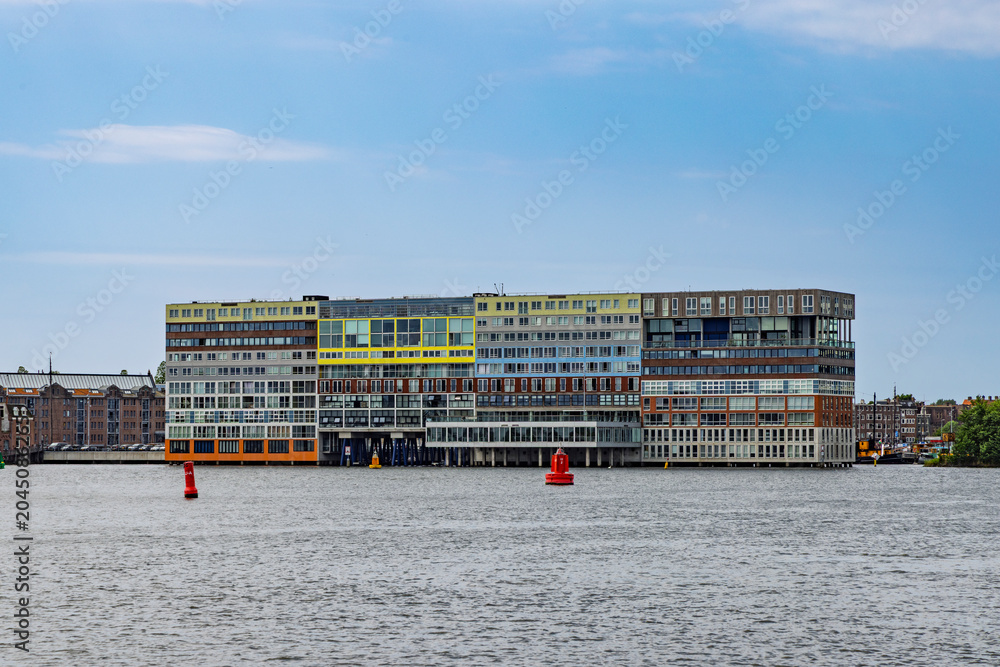 Obraz premium Amsterdam, Netherlands - The iconic and colorful Silodam apartment building standing directly in the water of the IJ river under a clear blue sky.