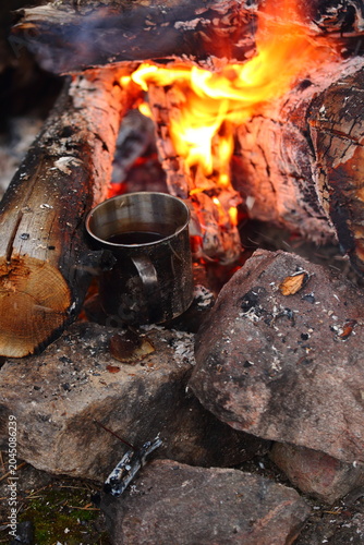 A mug of coffee is brewing in a campfire