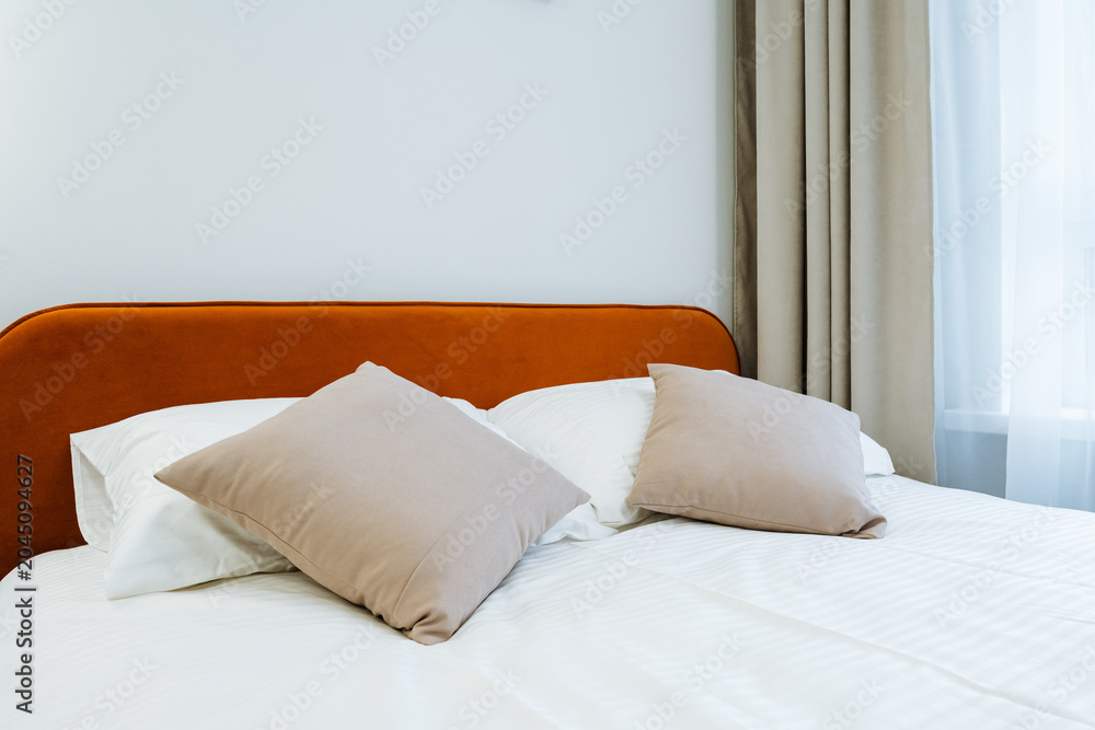 Obraz premium Minimal modern bed with rust-colored headboard and soft neutral pillows