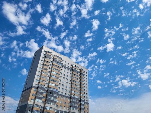 A high-rise apartment building against a bright blue sky with small white clouds