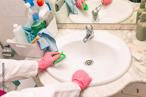 Someone wipes a white sink with a green scrub brush