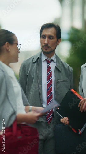 Three business professionals engage in a focused discussion, reviewing documents outdoors. The corporate team collaborates on strategic plans in an urban environment