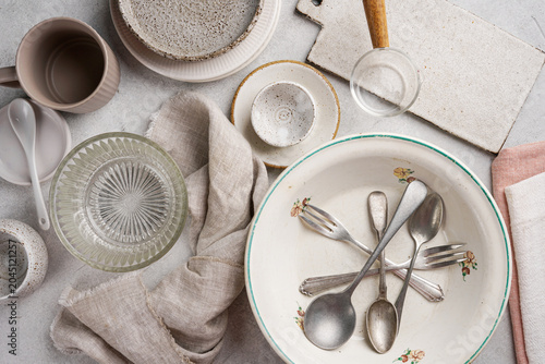 Vintage and rustic food styling props background. Ceramic plates, bowls, cups, silver spoons and linen napkins flat lay food photography on bright concrete table. Kitchenware banner template