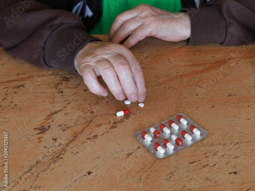 Elderly person's hands sorting medication tablets from blister pack on wooden table. Concept of aging, chronic illness, healthcare costs, expensive medicines and senior health management.