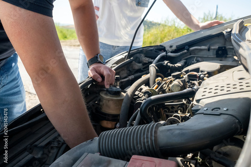 Bild auf Leinwand Person examining car engine under open hood due to vehicle breakdown on a road o